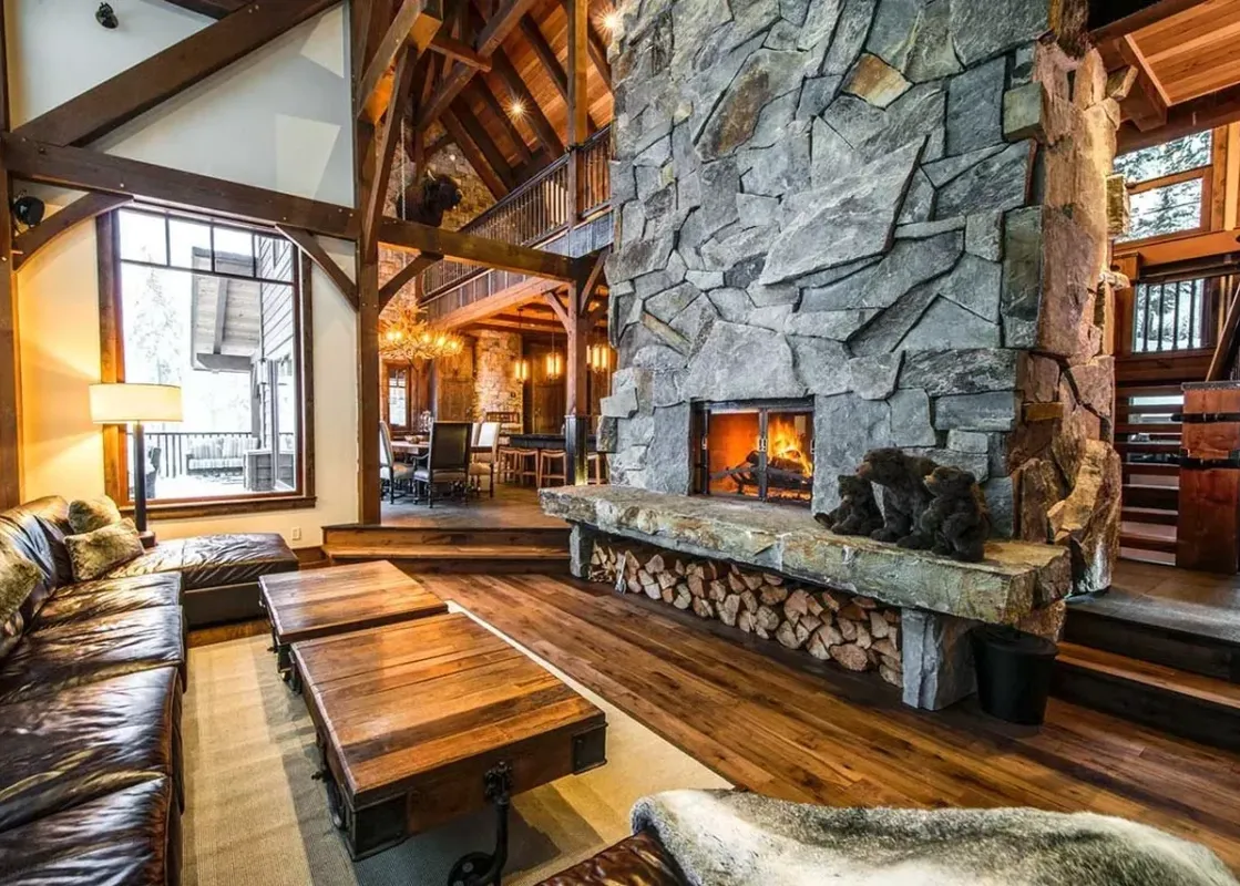 A large stone fireplace with a roaring fire in a rustic living room with a leather sofa and wooden coffee tables.