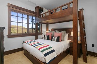 A cozy bedroom in Arrowleaf Lodge 205 with a queen bed, built-in wooden bunk beds, and a large window overlooking scenic hills.