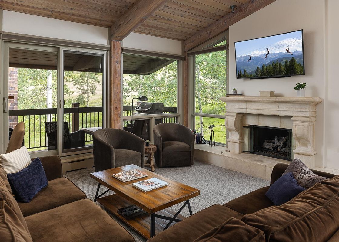 Top of the Village Slope 408 living area with a fireplace, large TV, and views of trees outside.