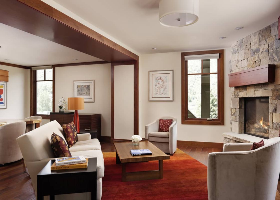 Living room with sofa, rich wooden floors, red area rug, fireplace, two grey armchairs