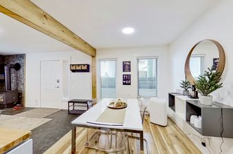 A modern dining room with a white table and chairs, wood floors, and a fireplace in the background.