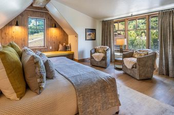 A serene bedroom at Ritz Carlton West Wing featuring a large bed with pillows, two armchairs by a window, and wooden walls.