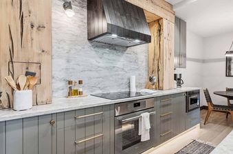 A modern kitchen with marble backsplash, gray cabinetry, stainless steel appliances, and rustic wood accents.