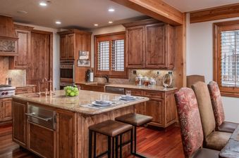 A modern kitchen with wooden cabinets, granite countertops, and stainless steel appliances. The kitchen has a large island with seating for two.