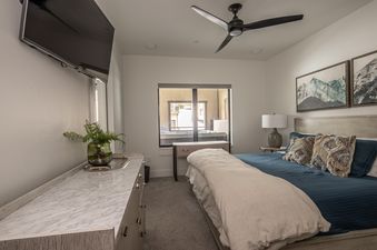 The primary bedroom features a modern design with a king-sized bed, a wall-mounted TV, and an exterior view through a large window.