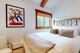 A cozy bedroom with a bed featuring a rustic branch headboard, white linens, and a vintage ski poster on the wall, offering a window view to the outdoors.