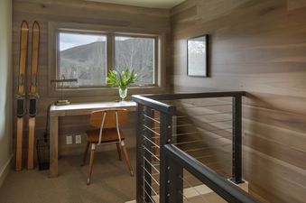 A wooden desk with a chair in front of a window with a view of snow-capped mountains.