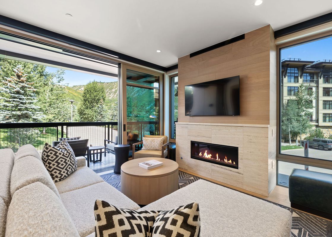 A modern living room at Assay Hill Lodge Unit 264 with a cozy fireplace, large sectional sofa, and expansive windows offering stunning mountain and architectural views.
