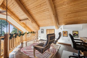 A cozy upper-level lounge with two recliners, a natural wood ceiling, and a railing adorned with garland overlooking an outdoor view.