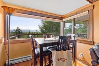 Cozy dining area at Snowridge 6 with scenic views of hills and pine trees through large corner windows.