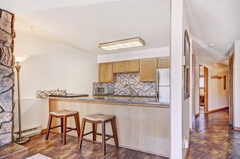 A kitchen in a condo rental with a breakfast bar and two stools, stainless steel appliances, and wood cabinets.
