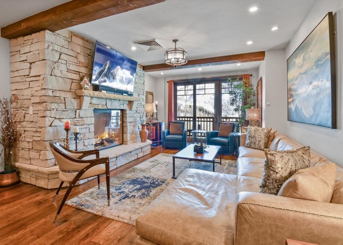 The warm and inviting living area of Silver Strike Lodge 201 203 featuring a prominent stone fireplace, comfortable leather seating, and mountain views through glass doors.