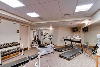 The Chateau Chamonix CX114's fitness center provides a range of equipment including treadmills, a recumbent bike, a multi-station weight machine, and a dumbbell rack, all set in a brightly lit room with mirrored walls and wall-mounted televisions.