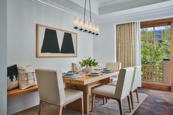 A modern dining area with a light wood table set with white and blue dishes, surrounded by cream-colored chairs and a built-in bench with decorative pillows.