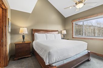 A bedroom with a large bed with white linens, two bedside tables with lamps, and a window with a view of a snowy forest.