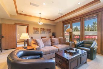 A living room with a large leather couch and two armchairs, a wooden coffee table with a tray on top, and a window with a view of the trees outside.