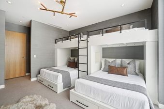 A modern bunk room in Founders Place 2403 with two custom-built bunk beds, each featuring a queen lower bed and a twin upper bed, against textured grey wallpaper.