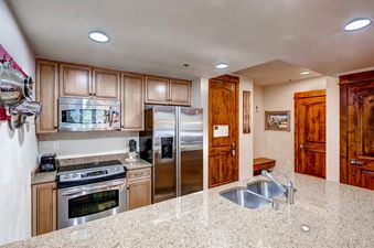 A modern kitchen with wooden cabinets, stainless steel appliances, and a granite island with a sink.