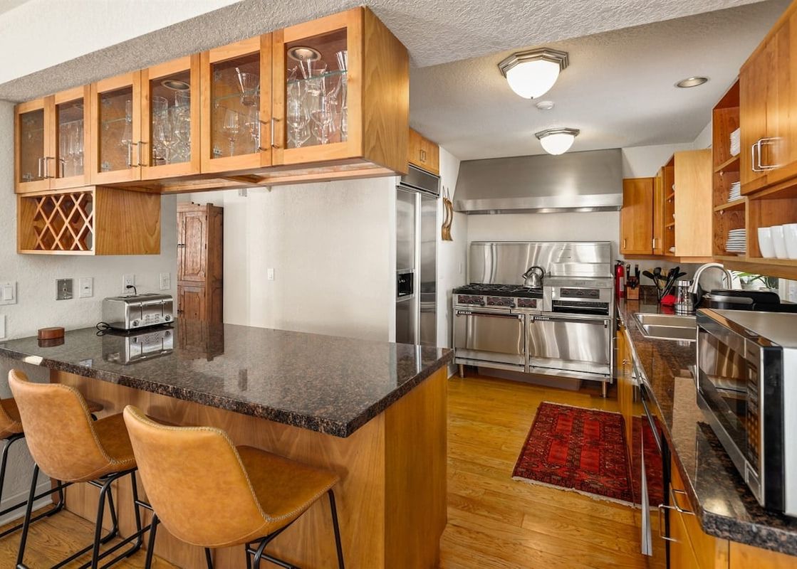 A modern kitchen with stainless steel appliances, light wood cabinetry, and a dark granite island with bar seating is illuminated by recessed lighting.