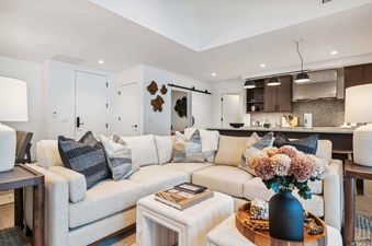 A modern living area with a large sectional sofa, coffee table, and a bouquet of flowers.