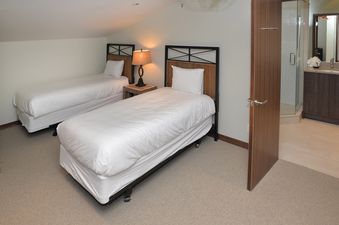Two single beds with white bedding are neatly arranged in a bedroom with a sloped ceiling and light-colored walls.