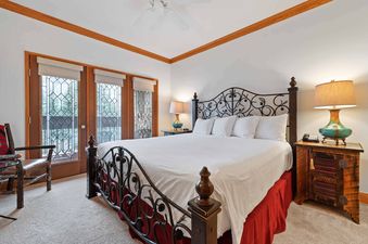 The primary bedroom in The Charter D2205 features a queen bed with a wrought iron frame, rustic nightstands, and French doors leading to a view of snowy pine trees.