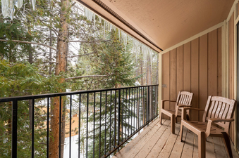 A close-up view of the balcony at Beaver Village 333 during winter, with two chairs facing a snow-covered forest and icicles hanging from the roof.