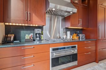A modern kitchen with dark wood cabinets, dark granite countertops, and stainless steel appliances, including a range hood, oven, and stovetop.