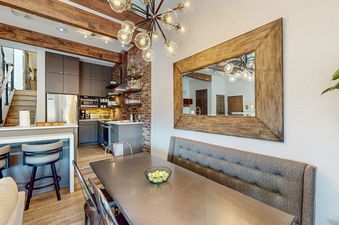 A dining room with a large wooden framed mirror, an exposed brick wall, and a metal table with green apples in a bowl