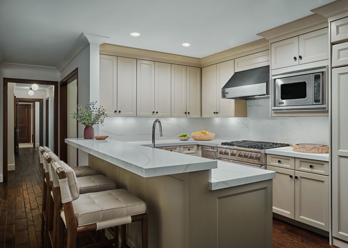 A modern kitchen with light colored cabinetry and dark wood floors.