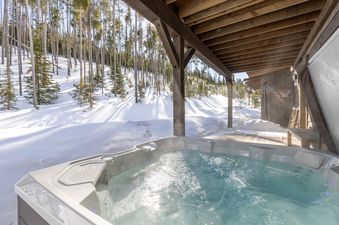 A bubbling hot tub on a snowy deck, surrounded by a winter forest, offering a luxurious outdoor experience at Spanish Peaks Highlands Cabin 36.