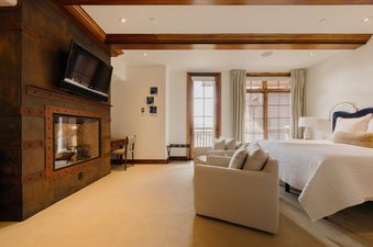 The Peaks Edge at See Forever provides a master bedroom, featuring a large king-sized bed, two armchairs, a fireplace with a flat-screen TV above, and large windows with mountain views.