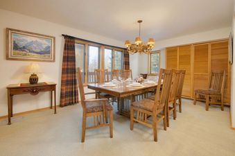 A warmly lit dining area at Windriver 1 with a large wooden table, matching chairs, and a mountain painting.