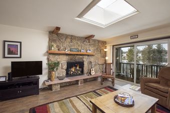 The inviting living area of Hi Country Haus 2115, featuring a cozy fireplace, comfortable seating, and a large window overlooking a snowy landscape.