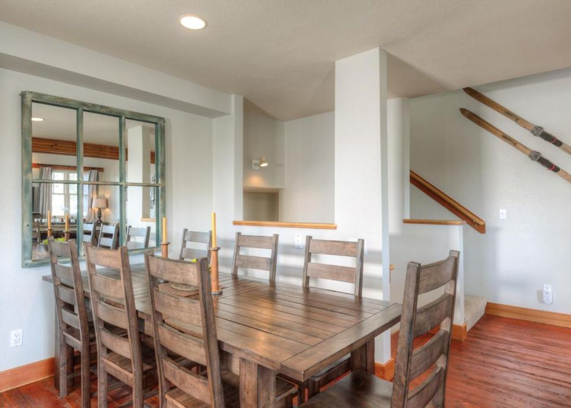 The dining area at Saddle Ridge Townhome Unit B1 features a large wooden table and chairs, with a rustic framed mirror on the wall.
