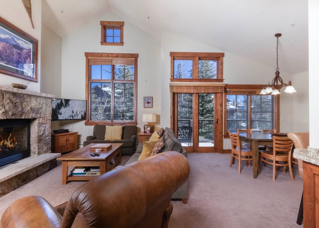The living area of the Villa at Mountain Thunder features a stone fireplace, comfortable seating, and large windows with views of the snow-covered trees.