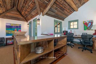 A rustic office space features a distressed wood vaulted ceiling, light-colored walls, and windows with green frames, offering a view of the outdoors.