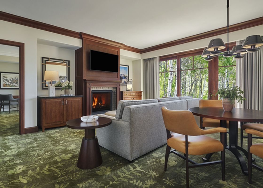 A spacious and elegantly furnished living room with a fireplace, comfortable seating, and a dining area, offering a view of the outdoors through large windows.