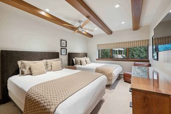 A spacious bedroom with two queen beds, a ceiling fan, wood beams, and a window with an exterior view.