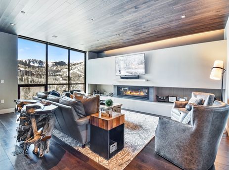 A modern living room at One Empire Pass 303 featuring large windows with mountain views, a linear fireplace, a wall-mounted TV, and comfortable seating.