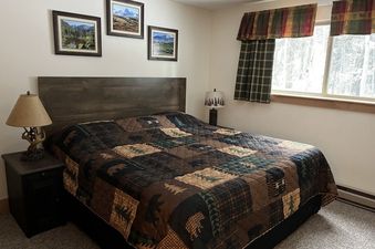 The bedroom at Beaver Village 414 features a queen-sized bed, a matching dark wood headboard and nightstand, and a warm, inviting quilt with bears and trees, creating a cozy, rustic retreat.