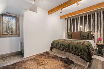 Cozy rustic bedroom in the Luxe Barnhouse featuring a birch-accented wall and wilderness-themed bedding.