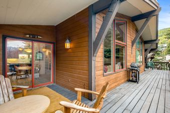 The All Seasons 2 Bedroom Gold Unit G3 features an expansive outdoor deck area with comfortable wooden seating and a grill, offering views of the surrounding natural landscape.
