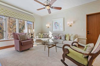 A cozy and inviting living room in The Charter D2805 with a large sectional sofa, two unique armchairs, round coffee tables, and large windows offering an exterior view of trees.