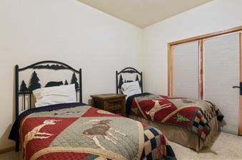 The secondary bedroom at Silvertip Ski Haus features two twin beds with nature-themed metal headboards and matching quilts, separated by a wooden nightstand.
