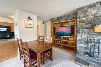 A dining table set with four chairs sits in front of a stone fireplace with a flat screen TV above it.