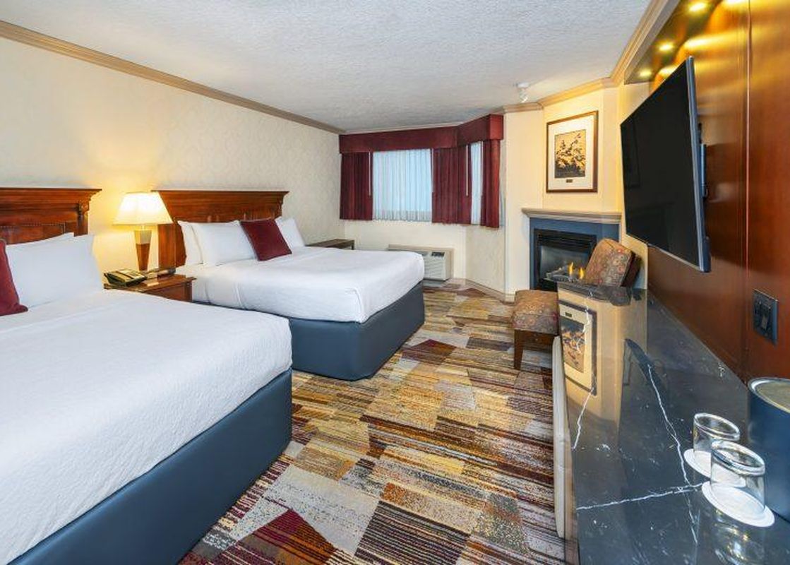 Two queen beds with burgundy accent pillows, a fireplace, and a wall-mounted TV are visible in the Royal Canadian Lodge Premier Room.