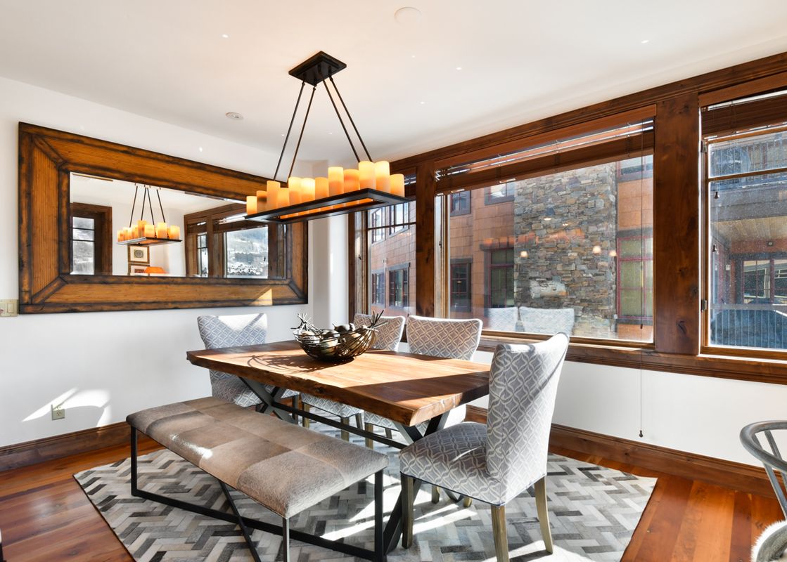 A dining area at Silver Strike Lodge 605 is elegantly appointed with a wooden dining table, a long bench, patterned chairs, and a large mirror reflecting the space.