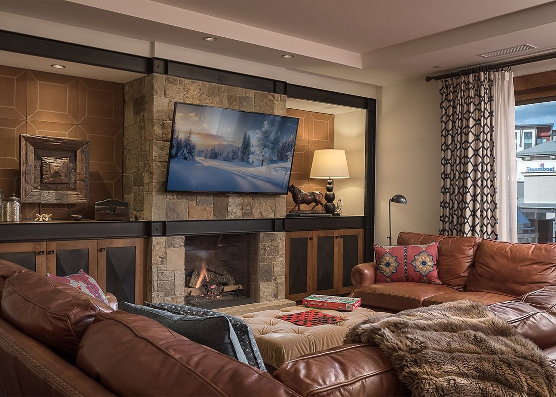 A cozy and luxurious living room with leather sofas, a stone fireplace, and a large TV, at Longs Peak One Steamboat Place 609.