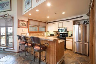 A well-equipped kitchen in Chateau Chamonix CX232 featuring modern appliances, granite countertops, and a bar with seating.